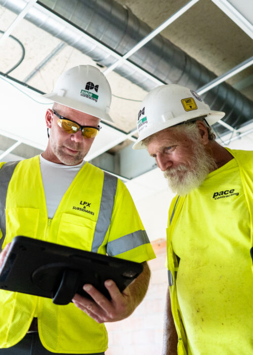 Two Pace contractors in hard hats and vests look onto a tablet in Kentuckiana