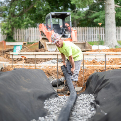 A Pace contractor lays a black pipe on gravel on a job site in Kentuckiana